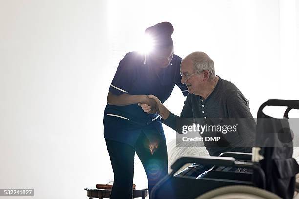 female nurse helping senior man get up from bed - backlit stock pictures, royalty-free photos & images