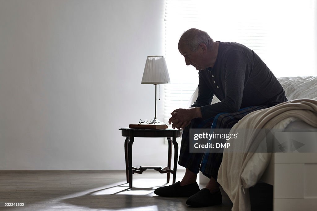Älterer Mann sitzt auf dem Bett, die ernsthafte