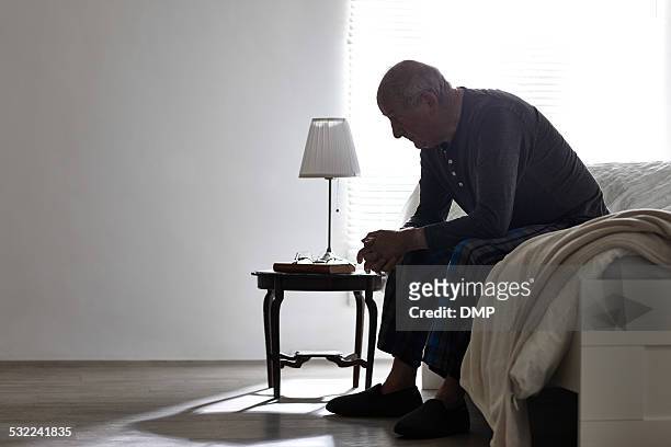 uomo anziano seduto sul letto guardando gravi - solitario foto e immagini stock