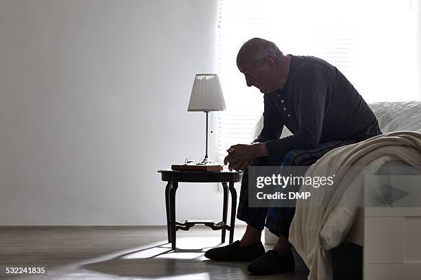 elderly man sitting on bed looking serious - smart stockfoto's en -beelden