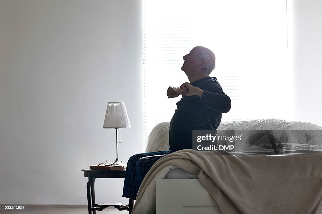 Uomo anziano seduto sul letto lo stretching le sue braccia