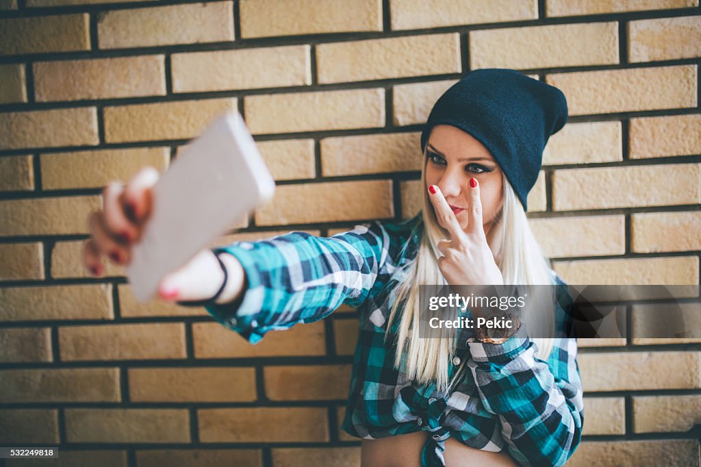 Emo Chica tomando autofoto contra muro de ladrillos