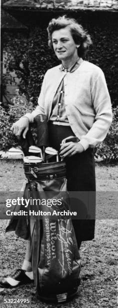 Legendary American athlete Babe Didrikson Zaharias stands on a field with a set of golf clubs with her name engraved on the bag, late 1940s. Zaharias...