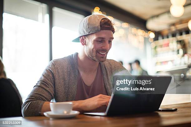 man using laptop in coffee shop - junger mann allein stock-fotos und bilder