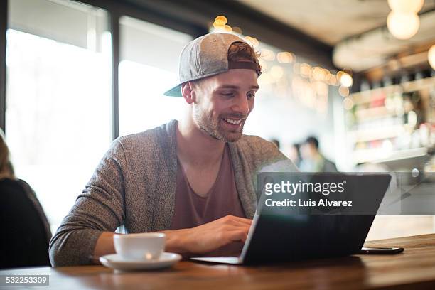 man using laptop in coffee shop - alleen één jonge man stockfoto's en -beelden