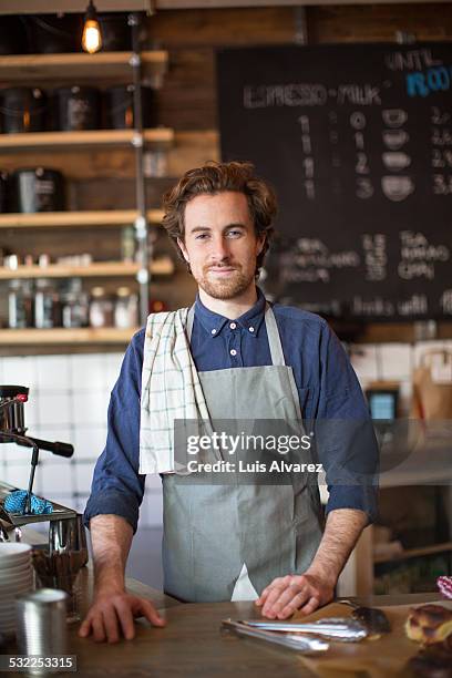 male barista standing at cafe counter - schürze stock-fotos und bilder