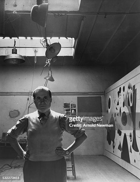 Portrait of Spanish artist Joan Miro as he poses, hands on his hips, in front of one of his paintings in Carl Holtya's studio, New York, New York,...