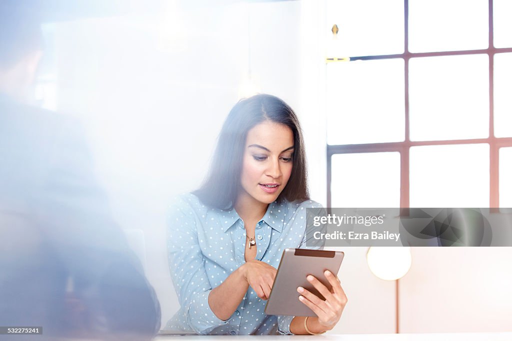 Young woman using a tablet in open plan office.