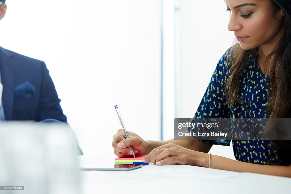 Businesswoman writing on post it notes in meeting.