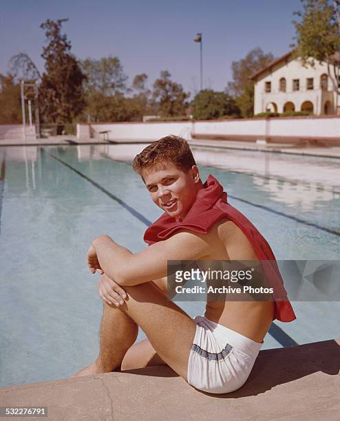 American film producer, director, actor, and sculptor Tony Dow sitting beside a swimming pool, circa 1965.