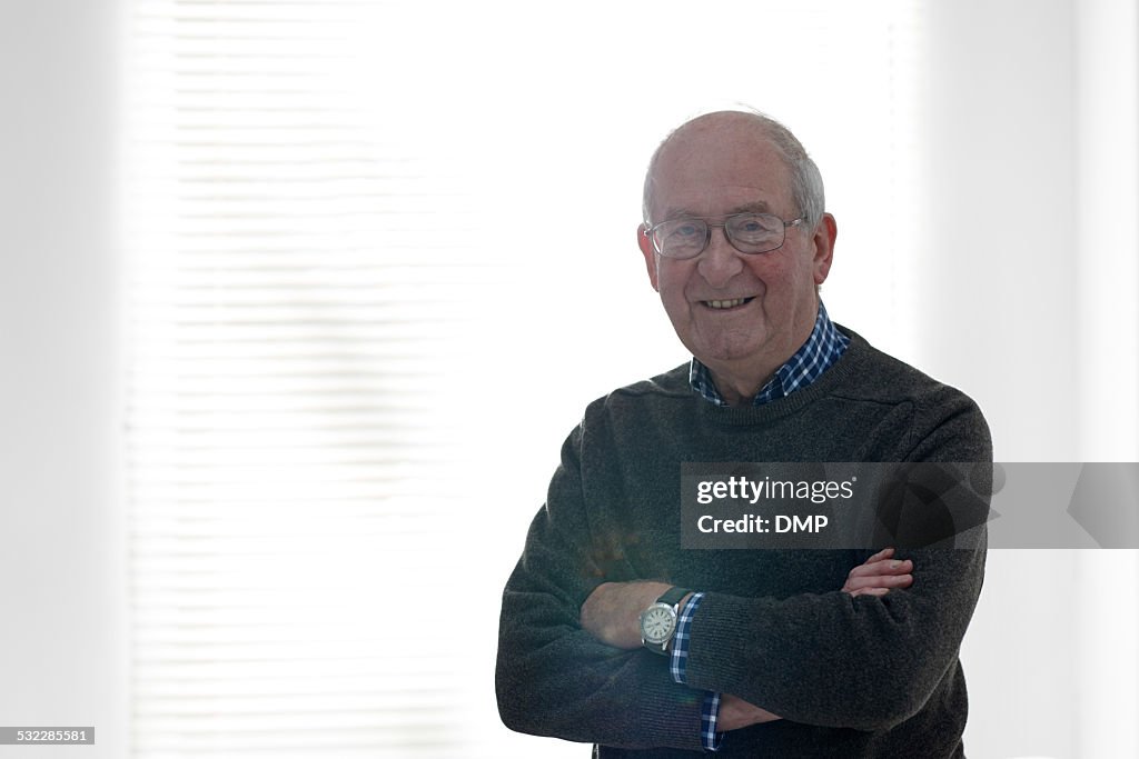 Senior man standing by a window looking happy