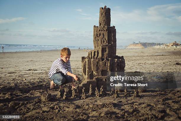 boy putting finishing touches on large sandcastle - kind sandburg stock-fotos und bilder