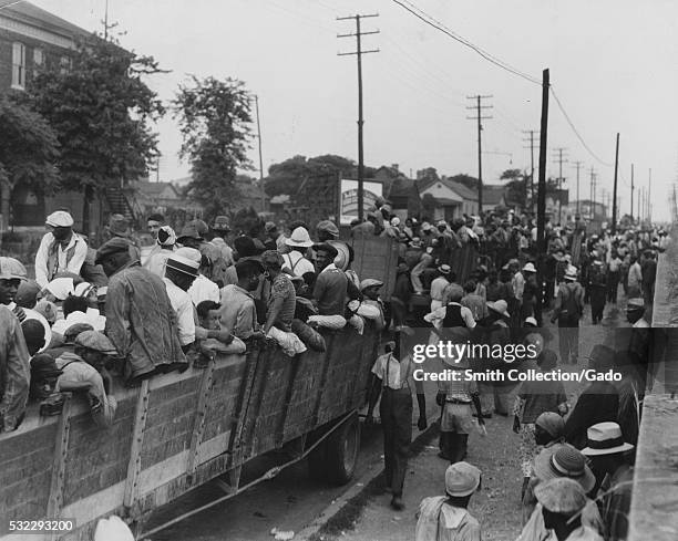Black and white photograph of a large group of cotton hoers loading into open wagons at Memphis for the day's work in Arkansas, June, 1937. From the...