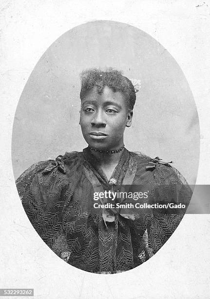 Photographic portrait of an unidentified woman, she is wearing a dark dress that has sheer lace covering the bodice, she is also wearing a choker and...