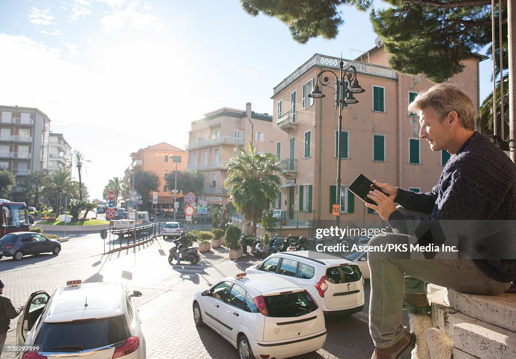 Man relaxes above town square, uses digital tablet