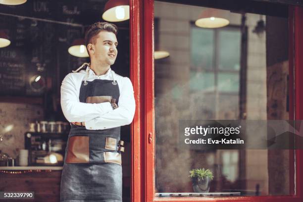 young waiter is standing at the coffee shop's entry - coffee shop owner stockfoto's en -beelden