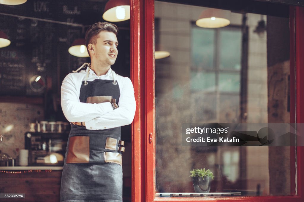 Young waiter is standing at the coffee shop's entry