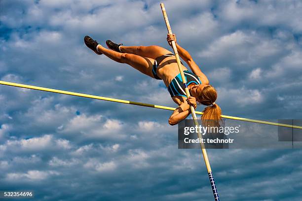 young women jumping over the lath against cloudy sky - mens pole vault stockfoto's en -beelden