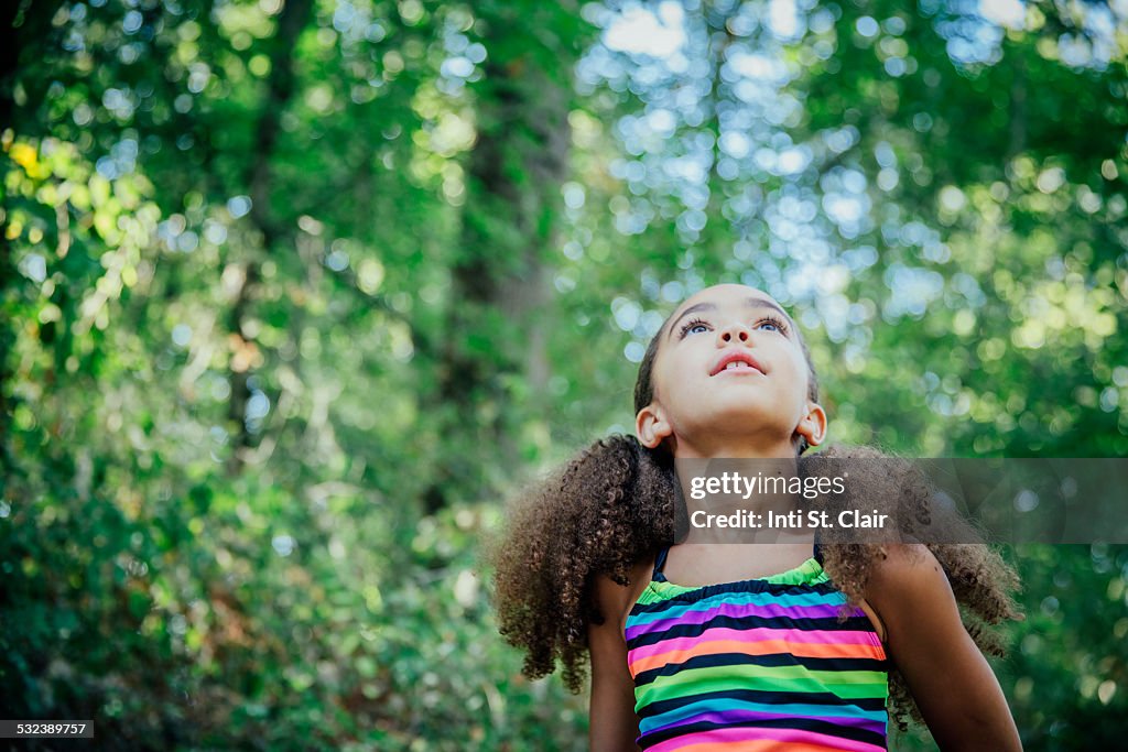 Mixed race girl outside looking up at trees