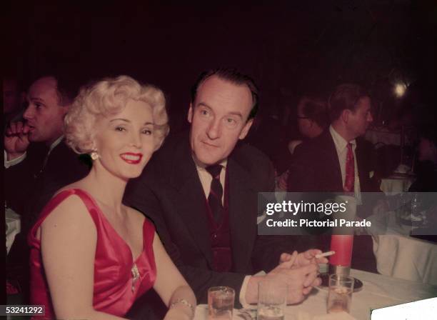 Hungarian actress Zsa Zsa Gabor smiles for the camera while sitting at a table with her husband, Russian-born actor George Sanders , 1950s.