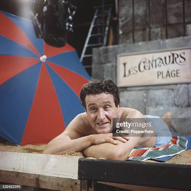 English actor Patrick Macnee pictured in character as John Steed wearing swimming shorts on the set of the television drama series The Avengers in...
