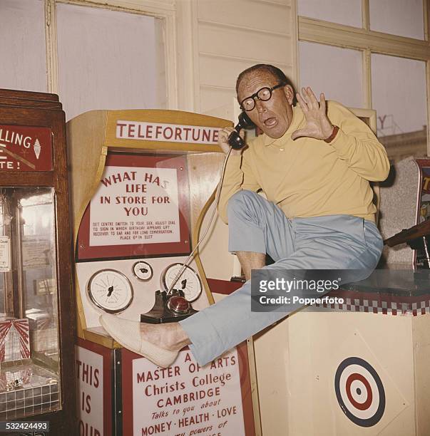 English actor and comedian, Arthur Askey pictured listening to a fortune telling machine in an amusement arcade at Southsea in England in 1963.
