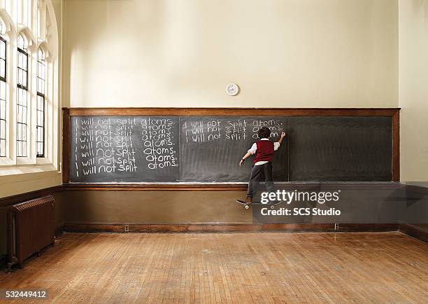 boy (8-9) floating on skateboard in classroom - wit blackboard stock-fotos und bilder