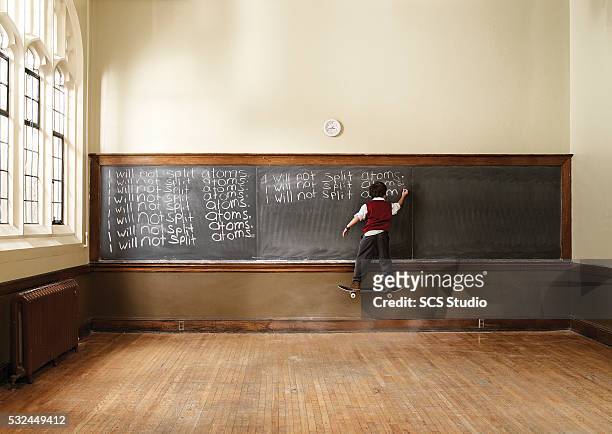 boy (8-9) floating on skateboard in classroom - wit blackboard - fotografias e filmes do acervo