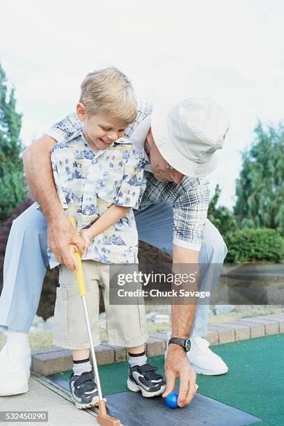 grandfather helping grandson at miniature golf - minigolf stockfoto's en -beelden