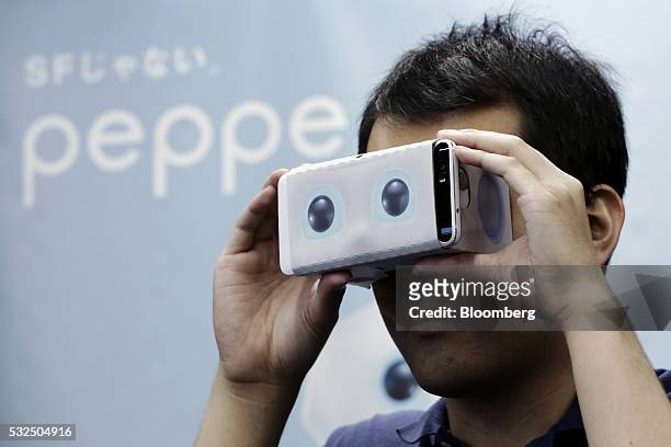 An attendant holds a Google Inc. Cardboard virtual reality headset to demonstrate SoftBank Group Corp.'s Pepper the humanoid robot at a media...