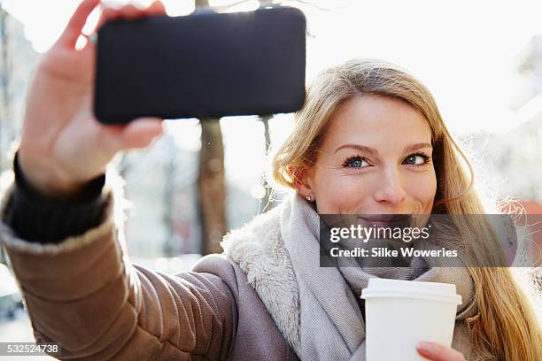 portrait of a content adult woman taking a self-portrait with her smartphone - blonde woman selfie foto e immagini stock