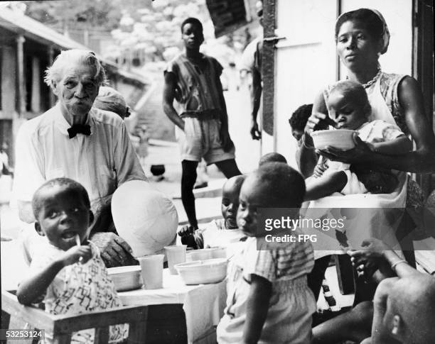 Alsatian-born German theologian, musician, physician, and medical missionary Albert Schweitzer sits at a table with young children as they eat a meal...