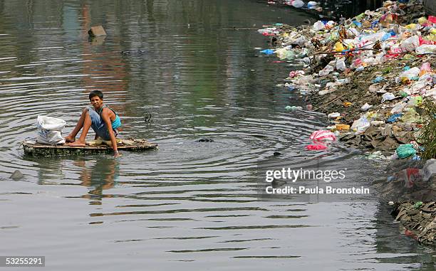 Filipino boy paddles a makeshift float in a polluted canal in the slums on July 19, 2005 in Manila, Philippines. Extreme poverty is commonplace in...