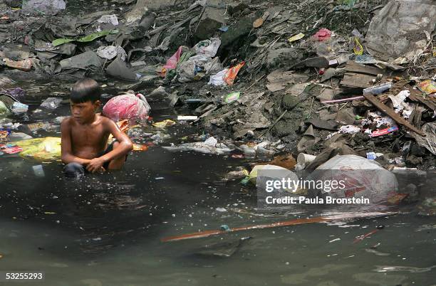 Filipino boy sits in a polluted canal in the slums on July 19, 2005 in Manila, Philippines. Extreme poverty is commonplace in Manila where...