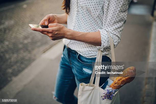 junge pariser frau benutzt dem smartphone - lady groceries phone stock-fotos und bilder