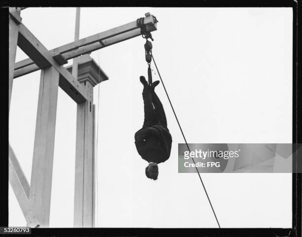 Hungarian-born American magician, escape artist, and psychic debunker Harry Houdini wears a straitjacket and hangs from a beam as he performs one of...