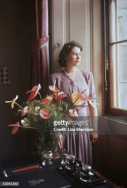 Princess Elizabeth, the future Queen Elizabeth II gazes through a window, near an exotic floral arrangement, 1946.