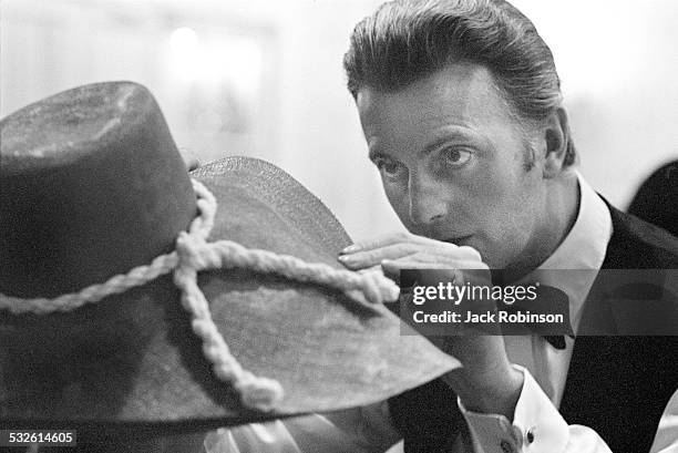 Portrait of designer Hubert de Givenchy as he adjusts a hat of his own design, 20th century.