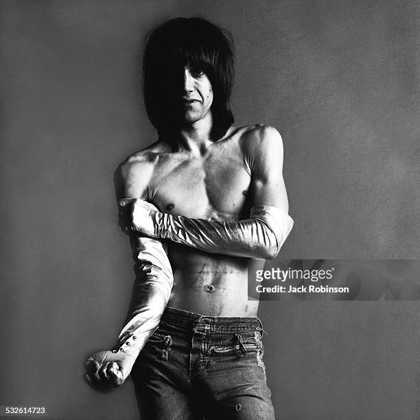 Studio portrait of American rock singer Iggy Pop, of the group the Stooges, barechested and in long satin gloves, as he poses with one arm extended...