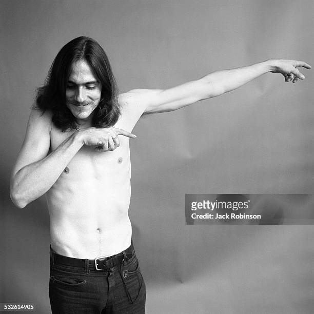 Portrait of American folk musician James Taylor, barechested, extending his left arm to his side, with his right arm held close and pointing to the...