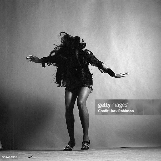 Full-length studio portrait of American rock singer Tina Turner, wearing a dark crocheted mini-dress, while looking down and stretching her arms out...