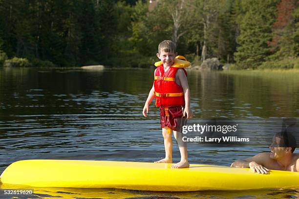 boy standing on a canoe being watched by his father - family red canoe stock pictures, royalty-free photos & images