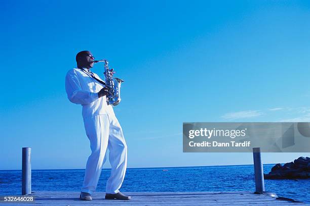 saxophonist playing on dock - saxophone stock-fotos und bilder