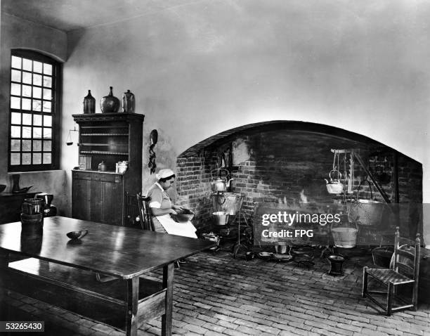 Woman in period costume, possibly playing the role of slave, sits with a mixing bowl by a large fireplace in the restored kitchen of the Lee family...