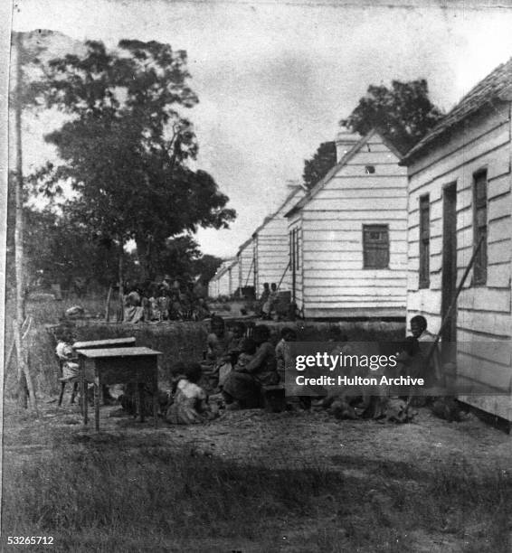 Group of slave children sit around behind the shacks in which they are forced to live on a plantation, South Carolina, 1860.