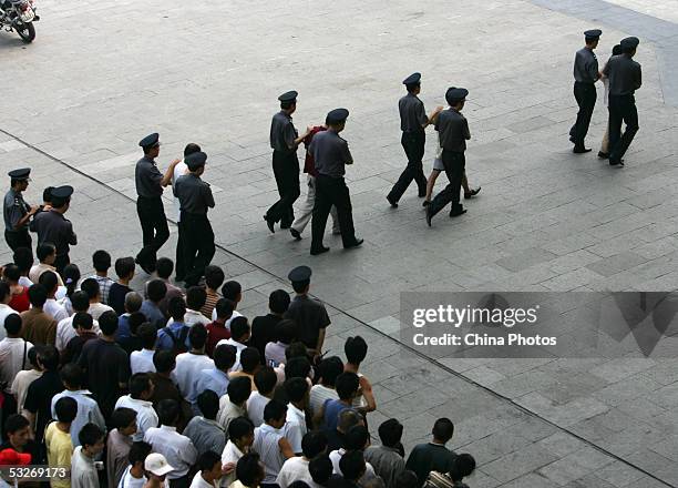 Police escort criminals being convicted of the illegal selling of train tickets as crowds watch during a public sentence at a railway station on July...