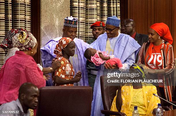 Nigerian President Mohammadu Buhari holds the daughter of the kidnapped Chibok schoolgirl Amina Ali as Borno state governor Kashim Shettima looks on...