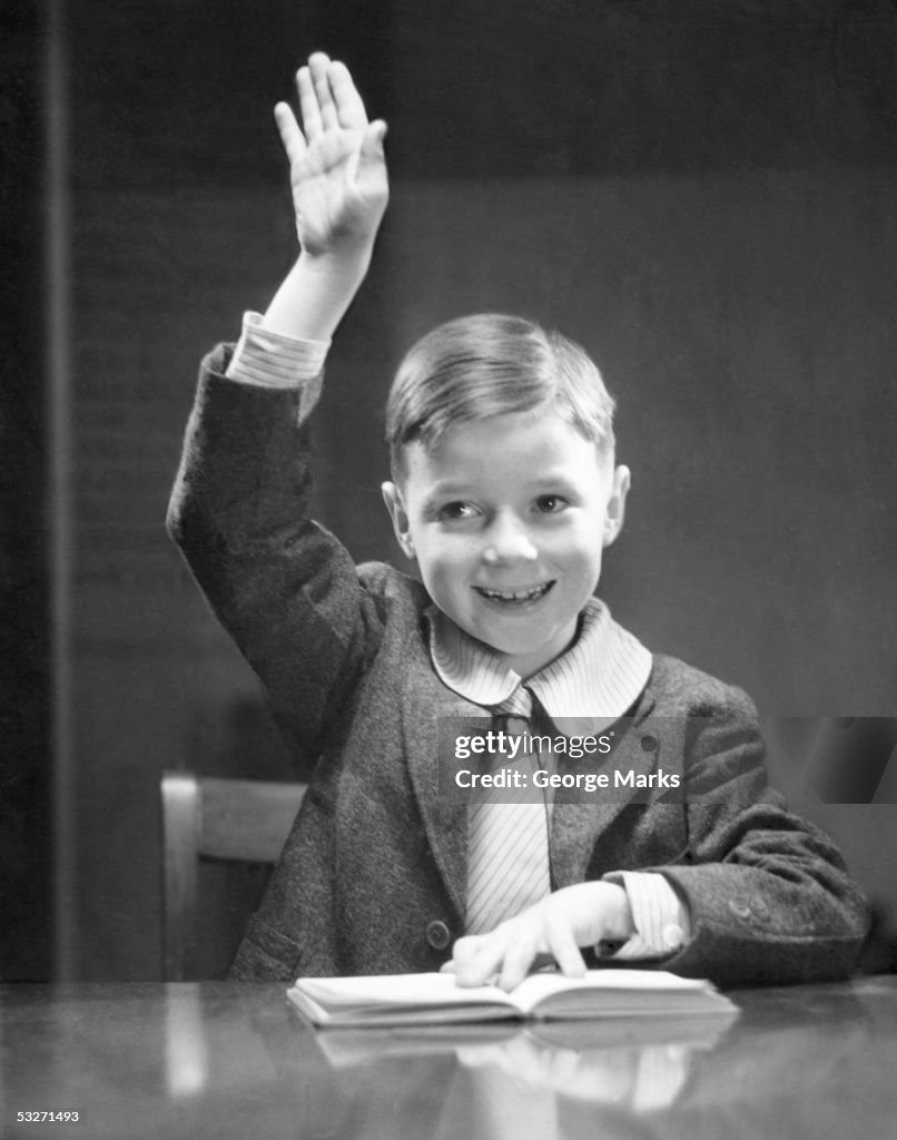 Boy at desk with hand raised