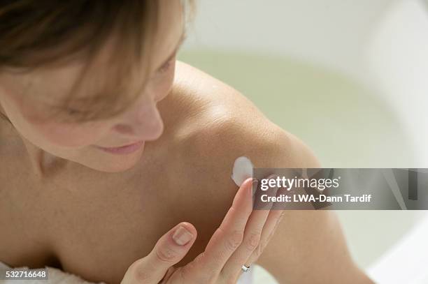 woman putting lotion on shoulder - body lotion stock-fotos und bilder