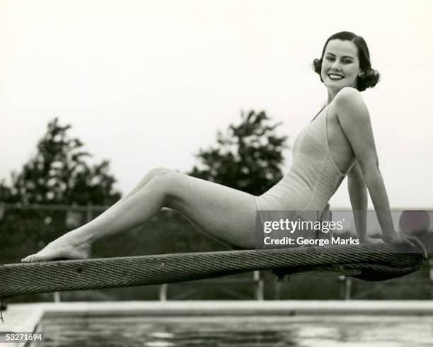 woman in bathing suit seated on diving board - women swimming pool retro stock-fotos und bilder